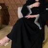 A lady wearing the Klassische Krepp-Abaya Zeitlos, seated gracefully, highlighting the silver and goldish patterns around the hands, elegantly paired with a watch.