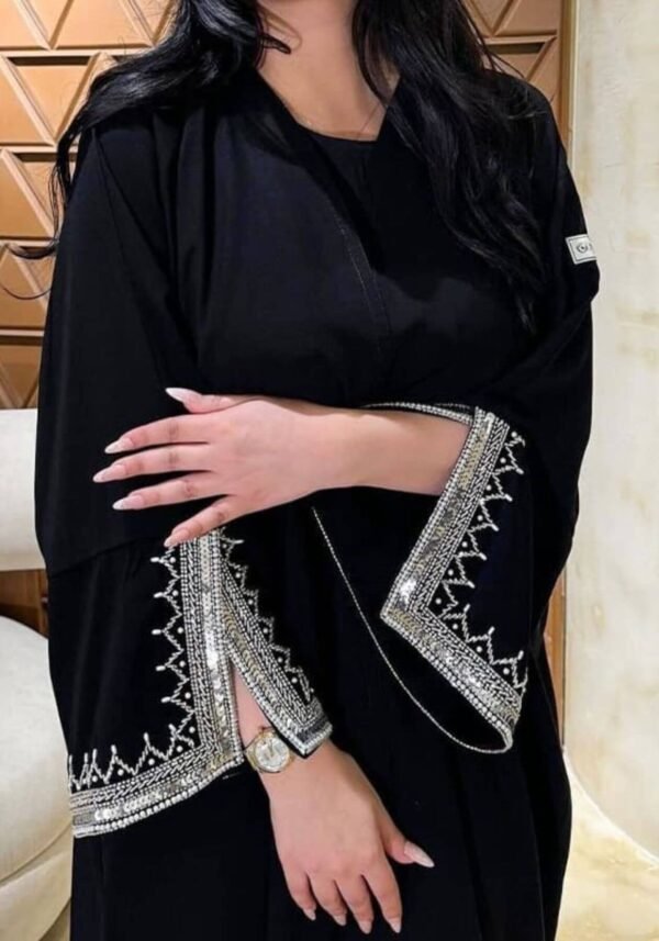 A closer front view of the Klassische Krepp-Abaya Zeitlos, showcasing intricate silver and goldish patterns around the hands, elegantly complemented by a watch.