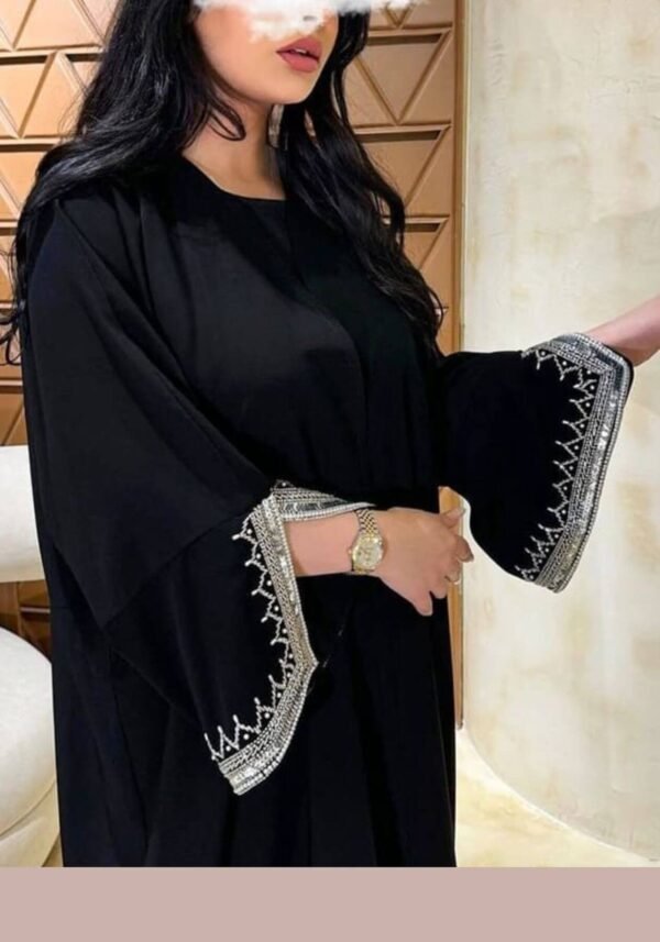 A lady wearing the Klassische Krepp-Abaya Zeitlos, a black abaya adorned with silver and goldish patterns around the hands, elegantly paired with a watch, highlighting timeless sophistication.