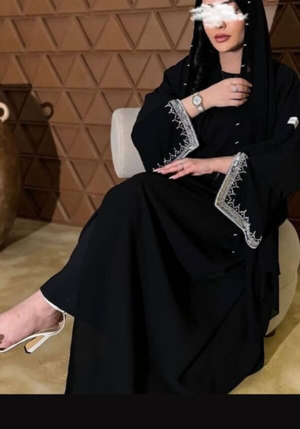 A lady wearing the Klassische Krepp-Abaya Zeitlos, seated gracefully, highlighting the silver and goldish patterns around the hands, elegantly paired with a watch.