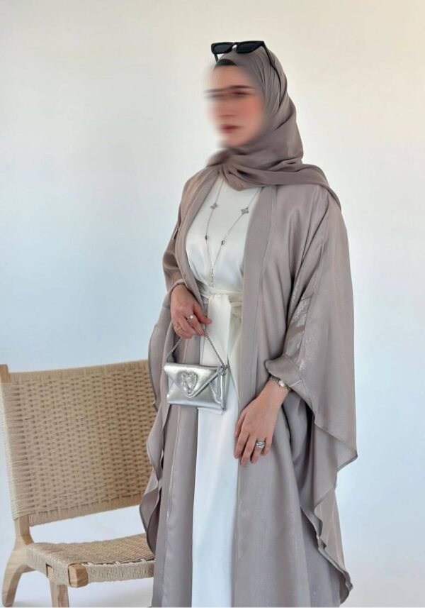 A lady wearing the Lexus Ensemble Vollkommenheit abaya with a beige interior, light brown exterior, and matching scarf, accessorized with a silver bag, exuding elegance and harmony.