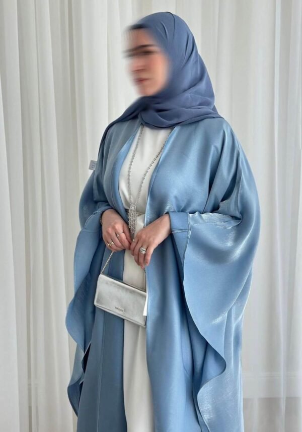 A lady wearing the Luxus Lexus-Ensemble Royal abaya, featuring a light beige and white interior with a light blue exterior, accessorized with jewelry and a silver bag, exuding modern sophistication.