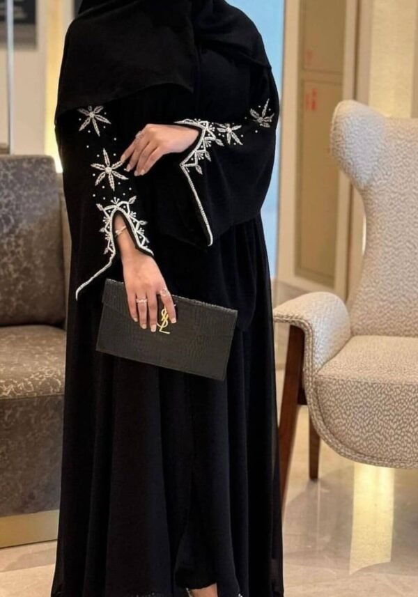 A lady wearing the Royal Chiffon-Abaya Leichtigkeit, a black abaya paired with elegant jewelry, holding a Yves Saint Laurent bag, showcasing luxury and sophistication.