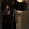 A lady wearing a luxurious abaya adorned with silver patterns, elegantly holding a stylish bag, exuding sophistication and grace.