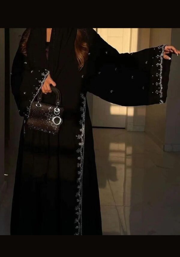 A lady wearing a luxurious abaya adorned with silver patterns, elegantly holding a stylish bag, exuding sophistication and grace.