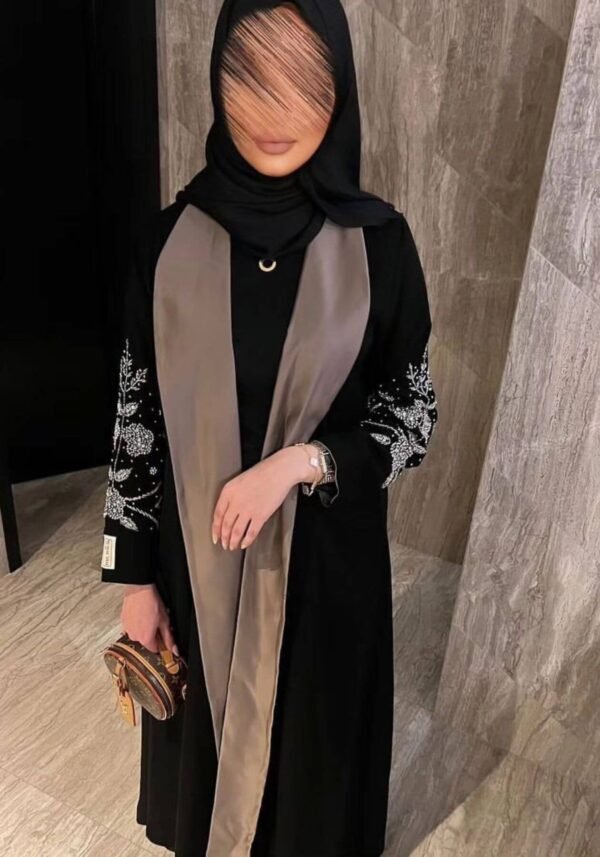 A lady wearing the Designer Krepp-Abaya Grace, featuring a flowerish pattern around the hand area and a light brown front design, elegantly paired with an LV bag.