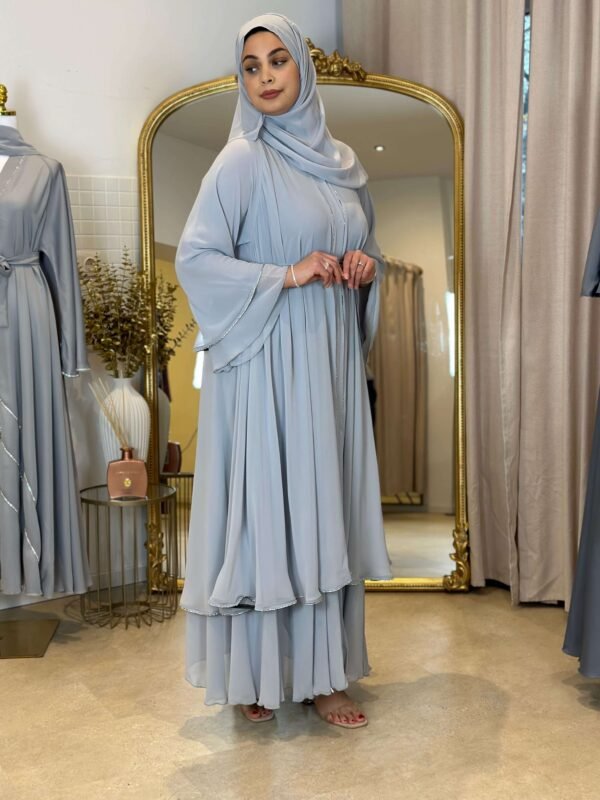 Eine Frau präsentiert die königliche Chiffon-Abaya in Himmelblau von der Seite, mit eleganten Akzenten und fließendem Schnitt.