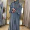 Präsentation einer graublauen Abaya vor einem goldenen Spiegel in einem stilvollen Showroom.