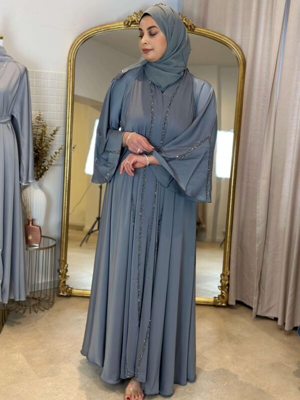 Präsentation einer graublauen Abaya vor einem goldenen Spiegel in einem stilvollen Showroom.
