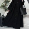 A lady wearing the Krepp-Abaya Essenz, an all-black abaya paired with a black bag and sporty sneakers, combining elegance with a casual touch.