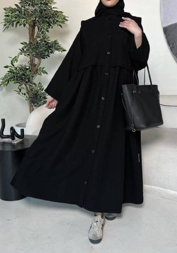 A lady wearing the Krepp-Abaya Essenz, an all-black abaya paired with a black bag and sporty sneakers, combining elegance with a casual touch.