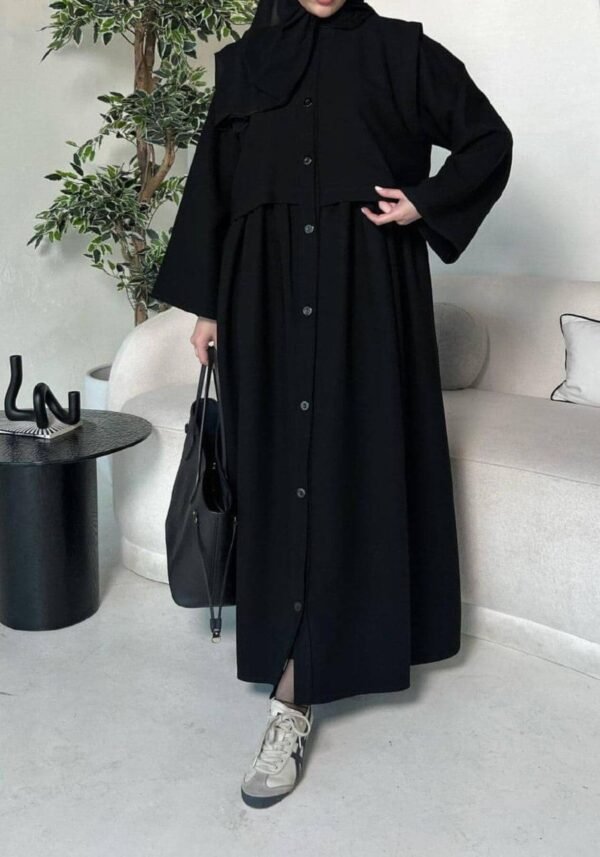 A lady wearing the Krepp-Abaya Essenz, an all-black abaya paired with a black bag and sporty sneakers, combining elegance with a casual touch.
