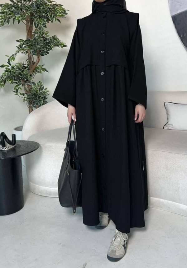 A lady wearing the Krepp-Abaya Essenz, an all-black abaya paired with a black bag and sporty sneakers, combining elegance with a casual touch.