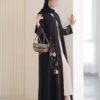 Eine Frau trägt die Royal Krepp-Abaya mit floralen Mustern und einer Designer-Tasche, präsentiert in einem modernen, stilvollen Ambiente.