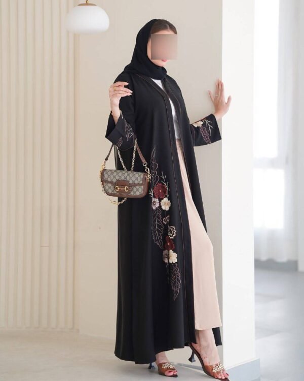 Eine Frau trägt die Royal Krepp-Abaya mit floralen Mustern und einer Designer-Tasche, präsentiert in einem modernen, stilvollen Ambiente.