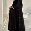 Eine Frau trägt die Royal Krepp-Abaya, ein zweiteiliges Set aus schwarzem Kreppstoff mit edlen Details, aufgenommen in einem modernen Raum.