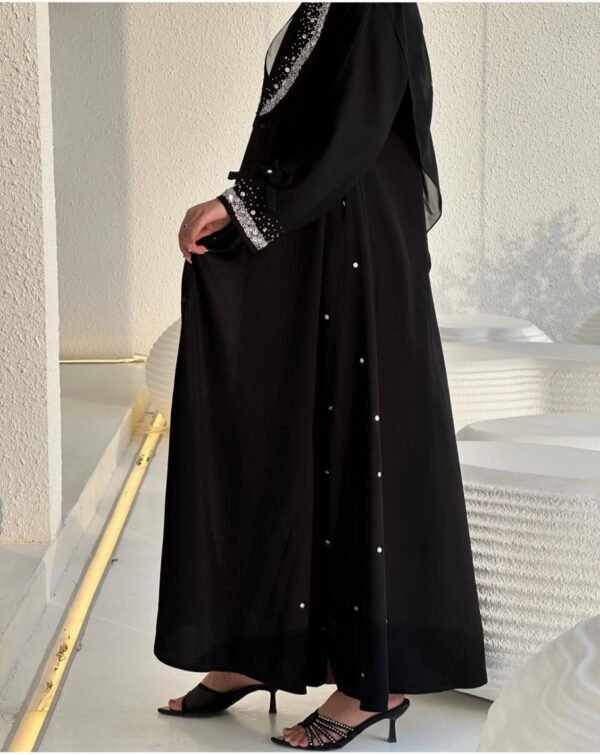 Eine Frau trägt die Royal Krepp-Abaya, ein zweiteiliges Set aus schwarzem Kreppstoff mit edlen Details, aufgenommen in einem modernen Raum.