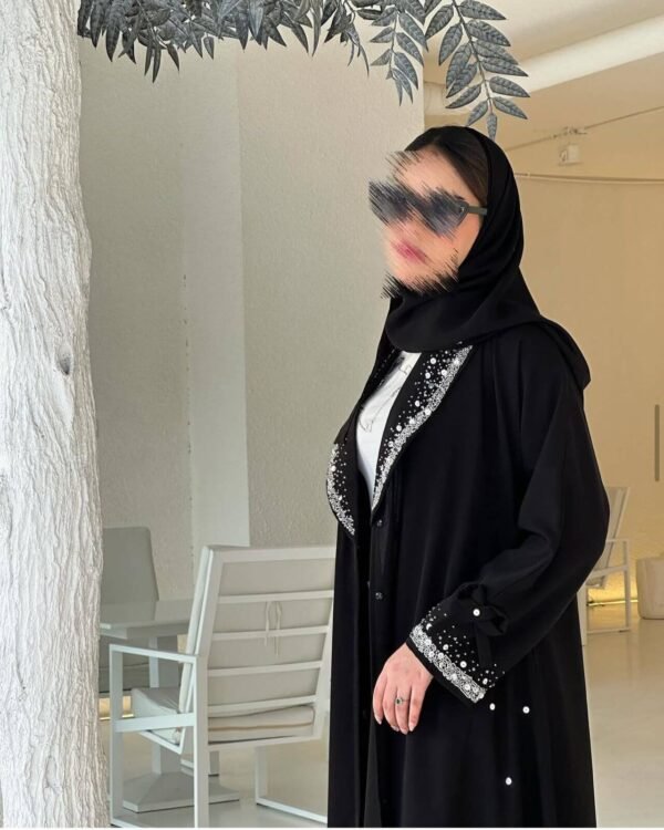 Eine Frau trägt die Royal Krepp-Abaya, ein zweiteiliges Set aus schwarzem Kreppstoff mit edlen Details, aufgenommen in einem modernen Raum.