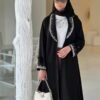 Eine stilvolle Frau in der Royal Krepp-Abaya, mit silbernen Verzierungen und einer weißen Tasche, zeigt die Eleganz dieses klassischen Designs.