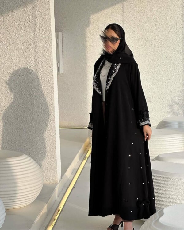 Eine Frau präsentiert die Royal Krepp-Abaya in einer vollständigen Vorderansicht, die das luxuriöse Design und die feinen Details hervorhebt.